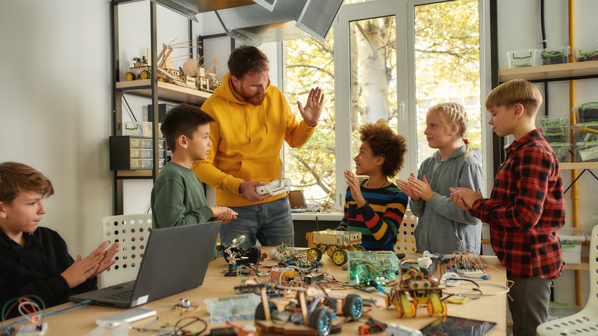 Working process. Young creative male teacher explains for students the principle of robotic machines work while holding console controller. Science and education.